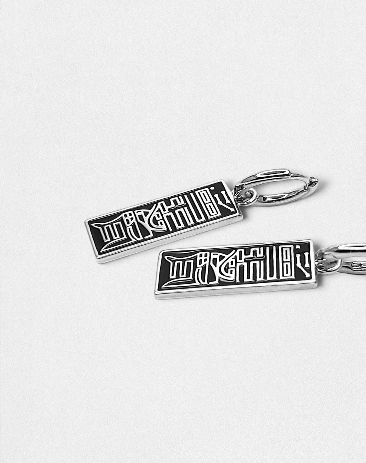 Close-up of silver 925 drop earrings, showing the black lacquer inlay and talisman details.