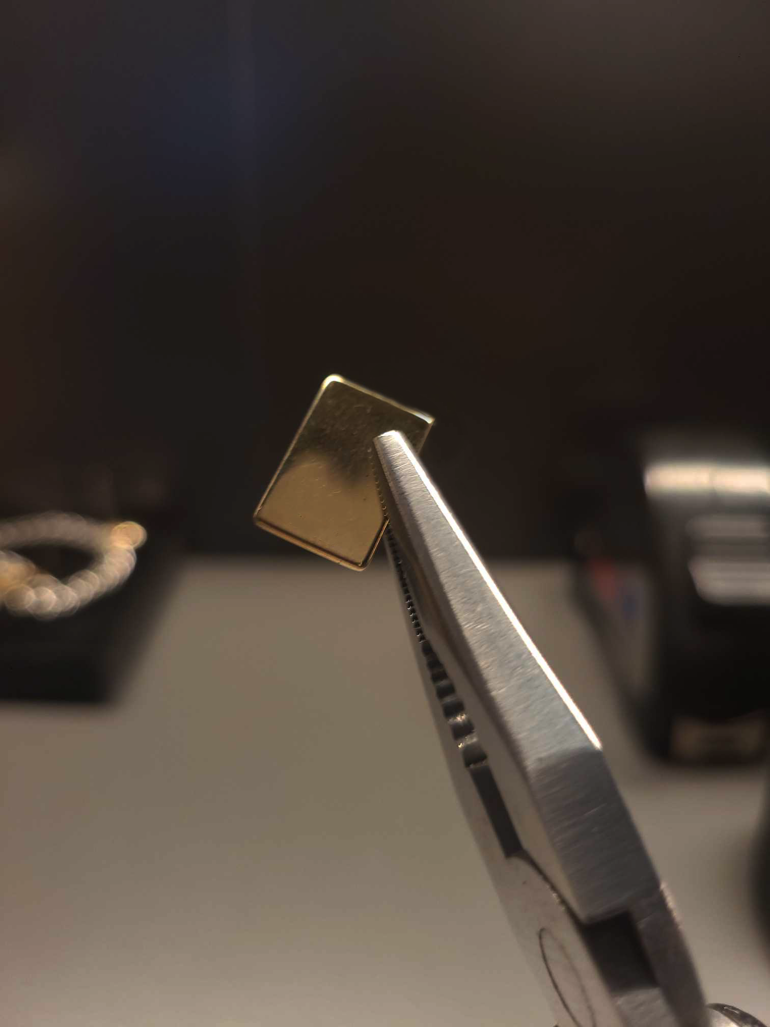 Pliers holding a rectangle piece of gold metal