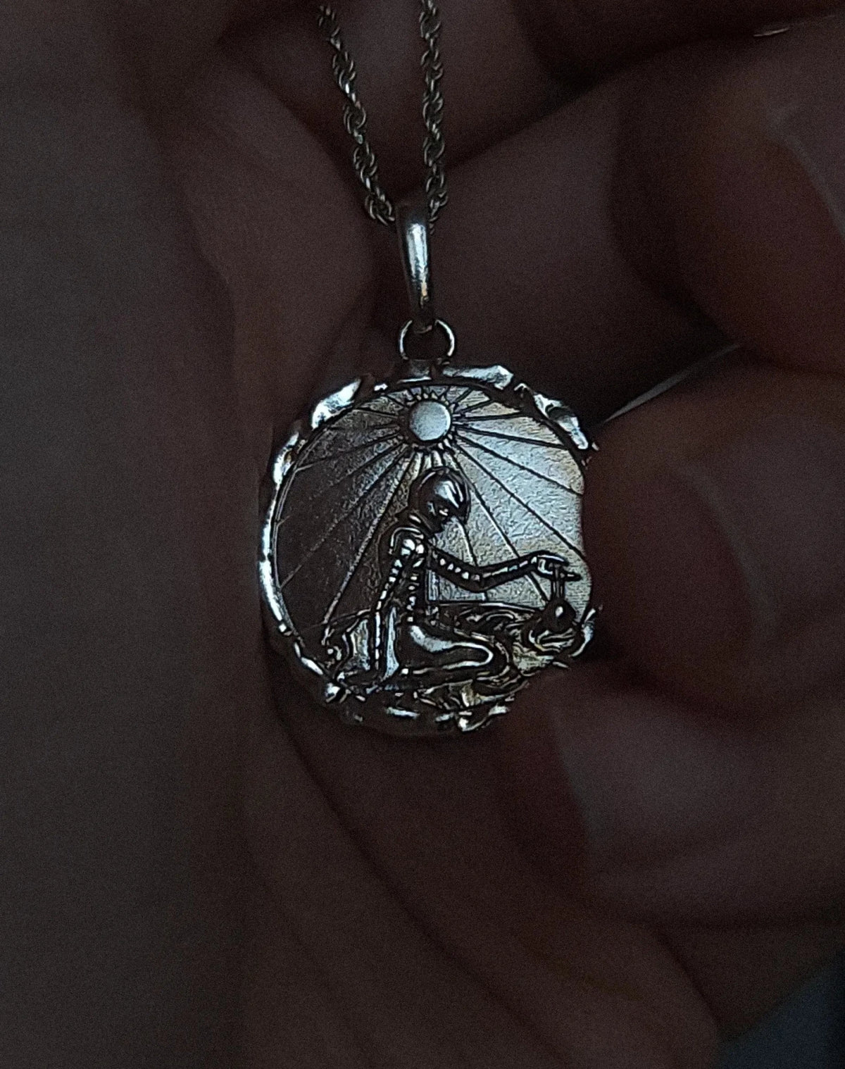 Silver Eclipse pendant necklace held in hand, showing shading and contrast on the design.